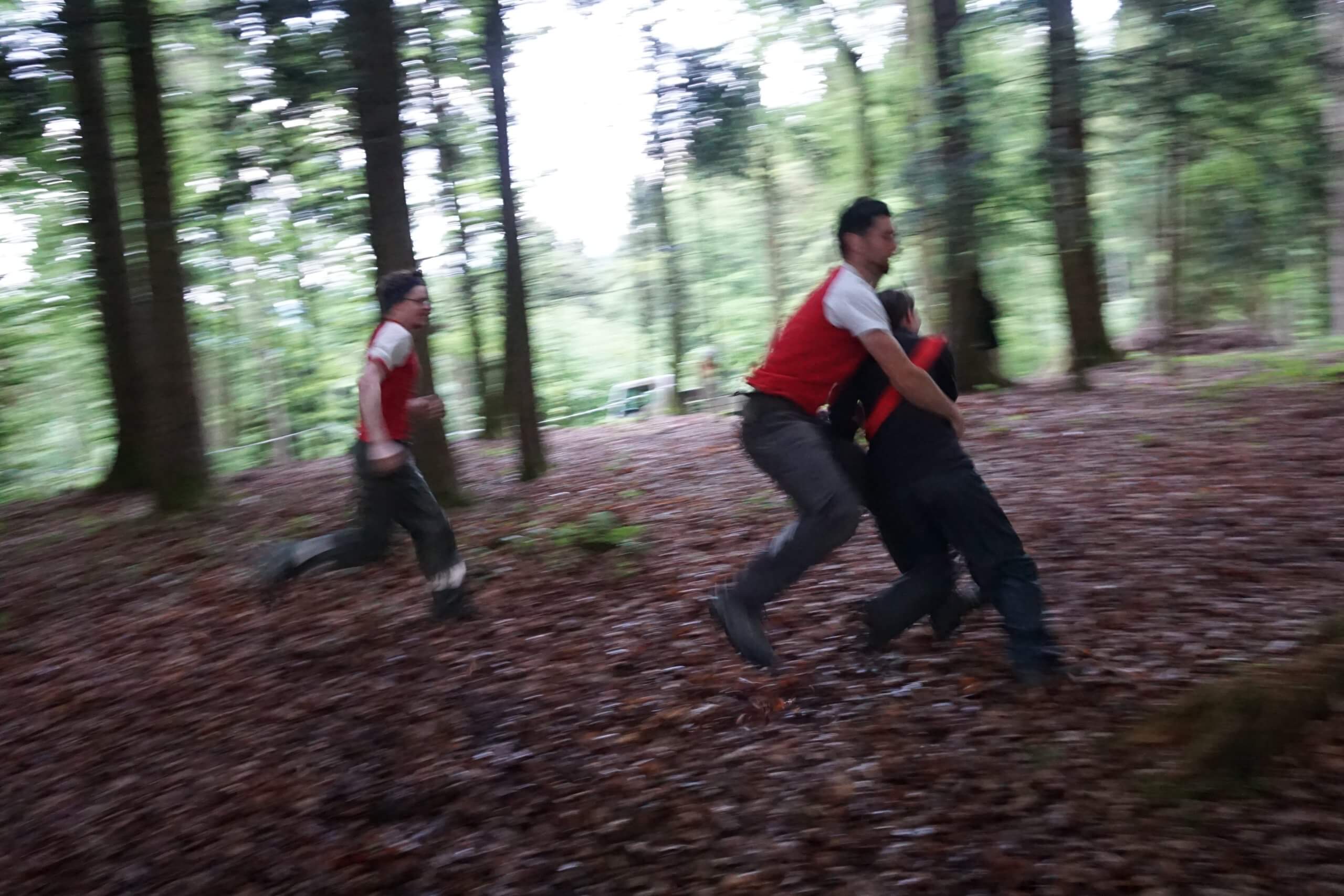 Three people running through a forest path in red vests, motion blurred.